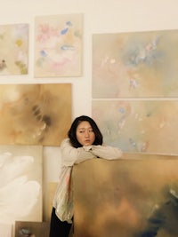 a woman leaning against a wall in front of paintings